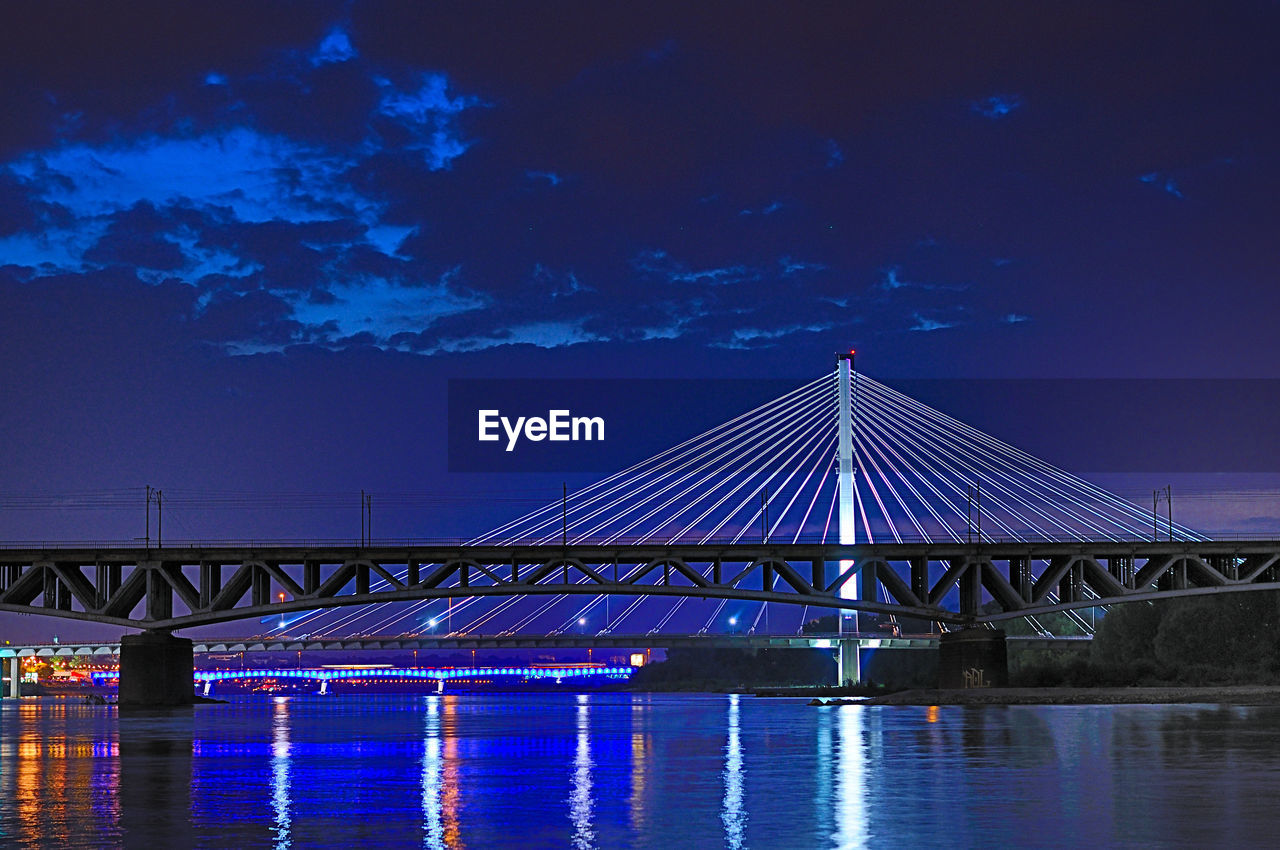 Illuminated bridge over river against sky at night