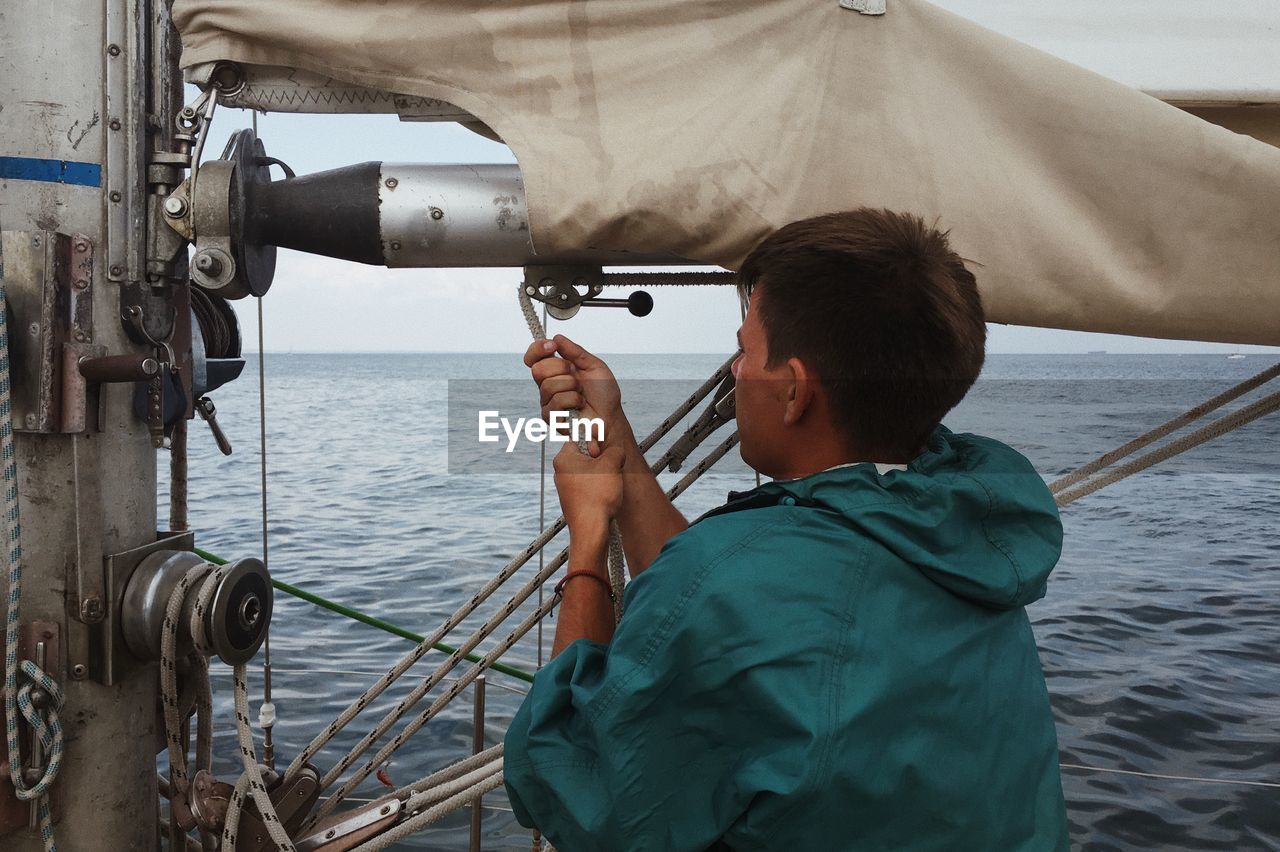 Man pulling rope in boat over sea