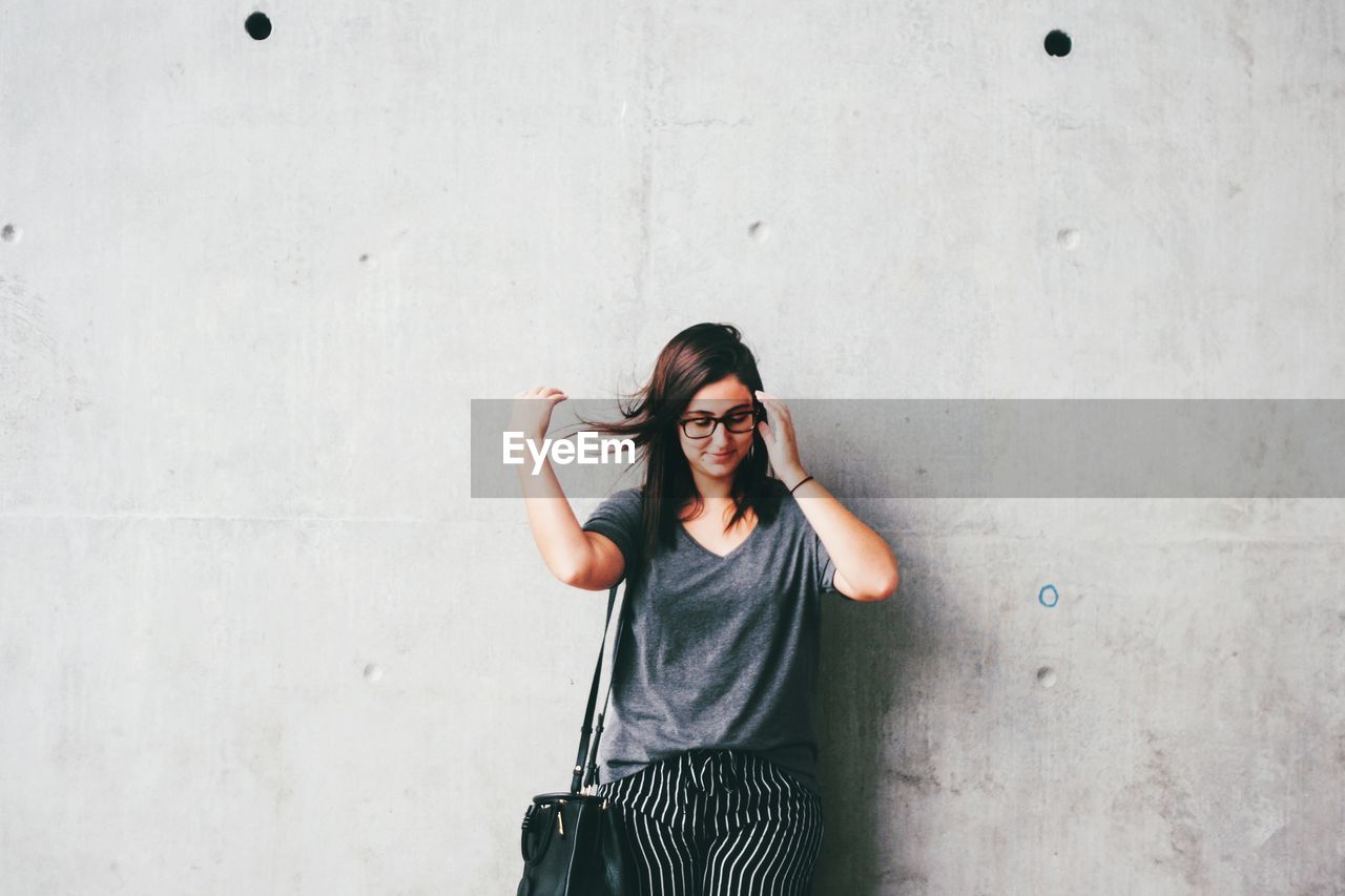 PORTRAIT OF YOUNG WOMAN STANDING AGAINST WALL