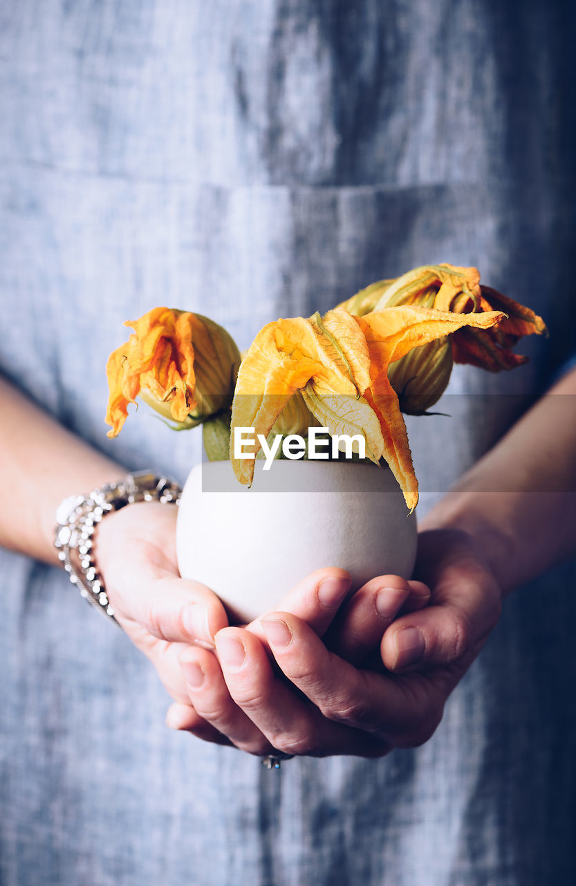 Midsection of woman with flowers in bowl standing indoors