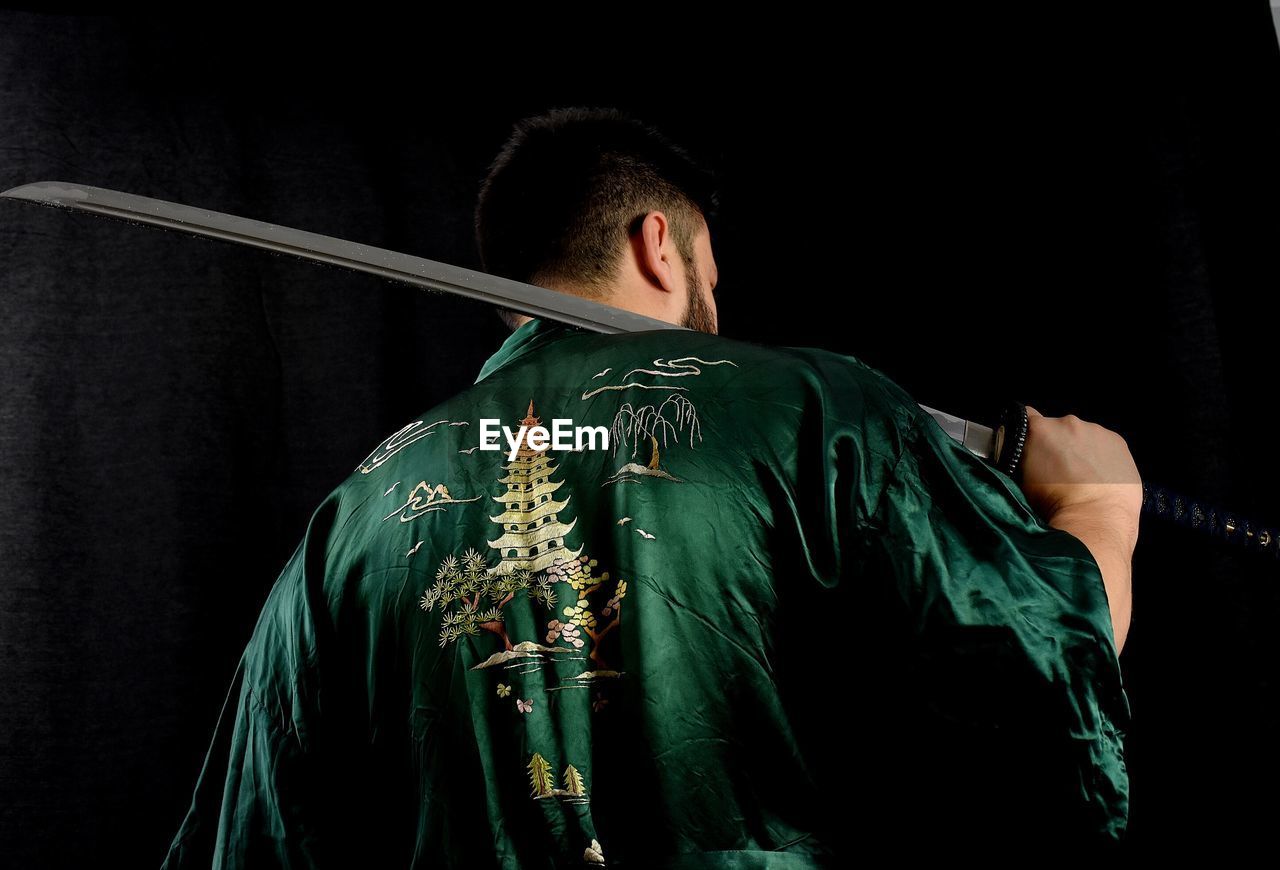 Rear view of man holding sword against black background