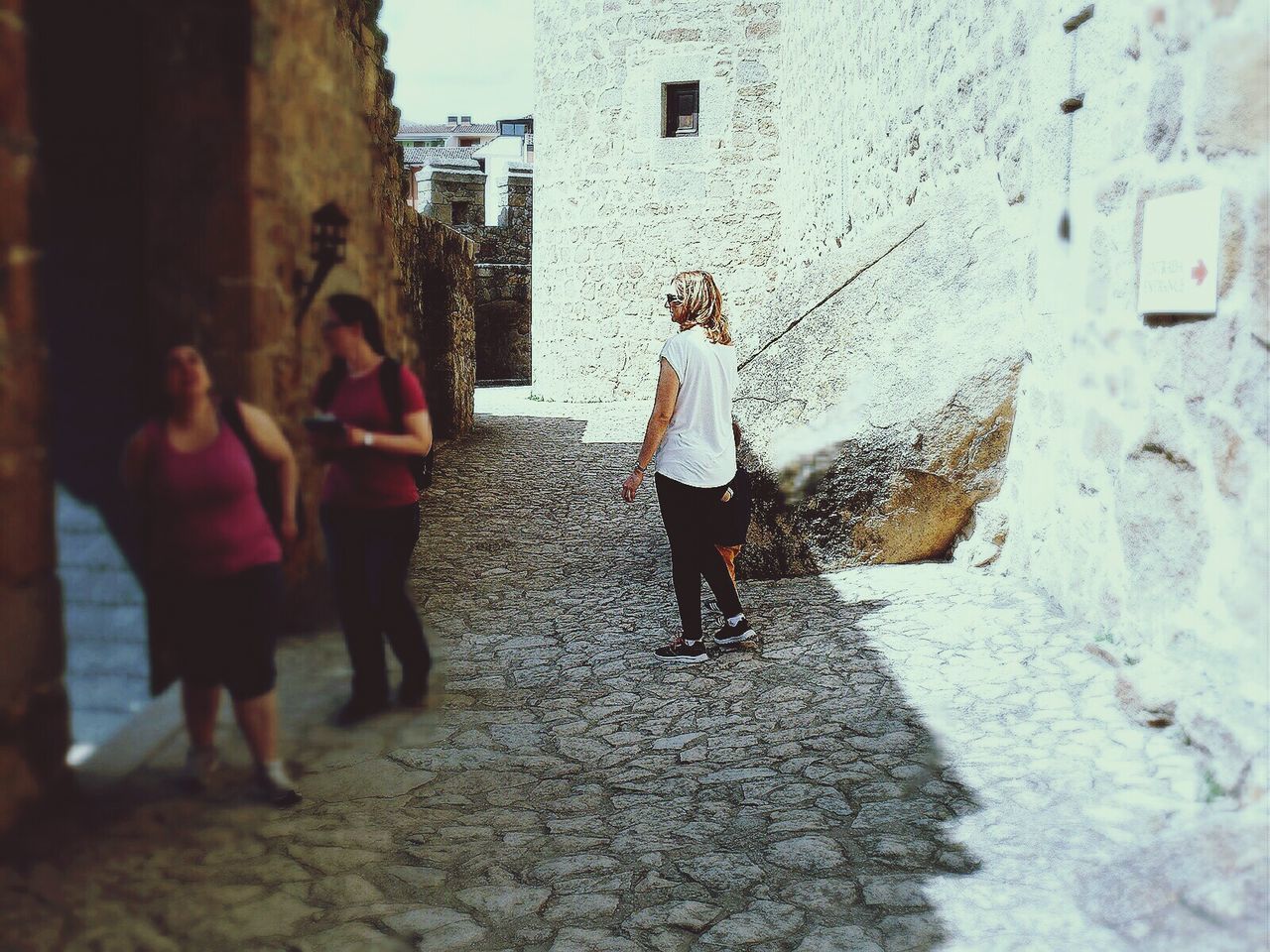 REAR VIEW OF PEOPLE WALKING ON COBBLESTONE STREET