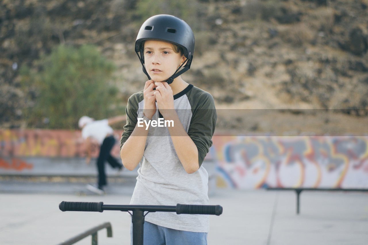 Teenager with helmets ready to ride his scooter on the skate park with friends. young sporty boy