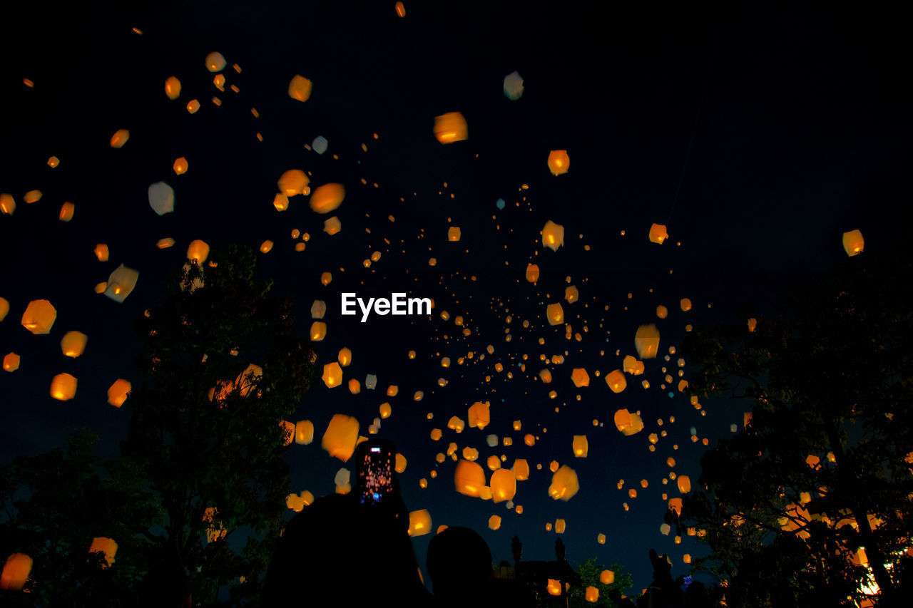 Low angle view of illuminated paper lanterns flying in sky at night