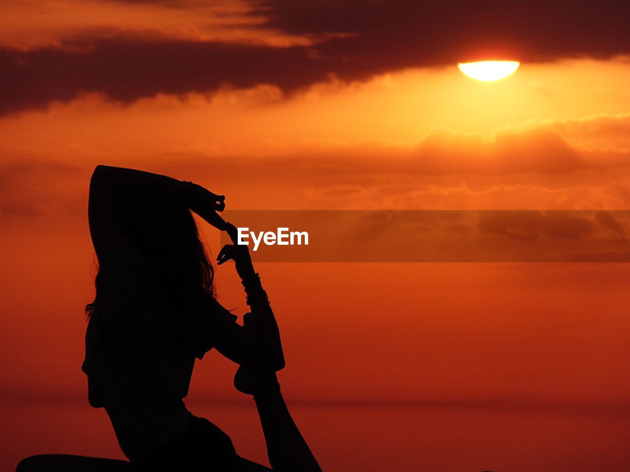 Silhouette woman exercising orange sky during sunset