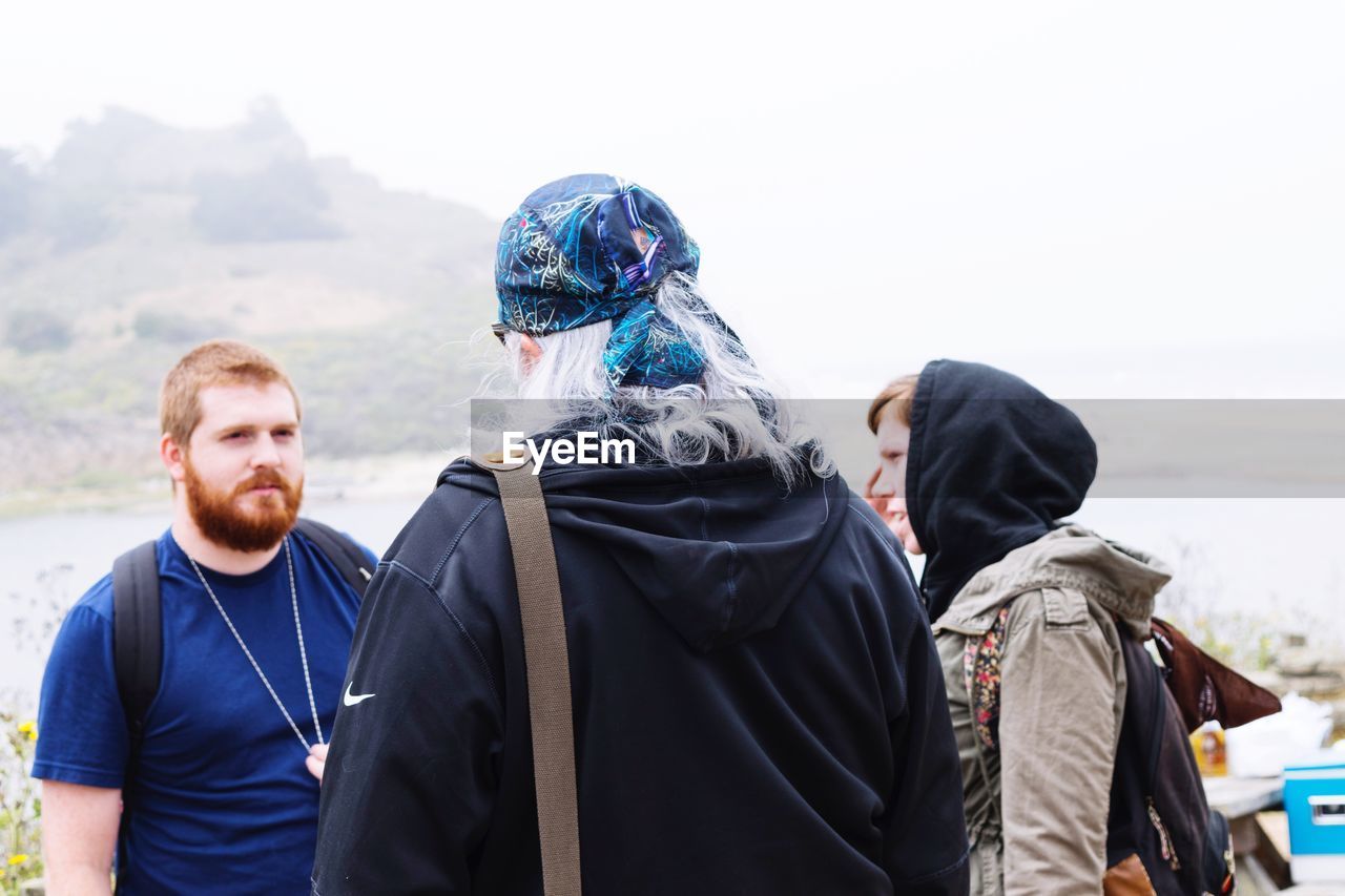 Friends hiking by mountain against sky during foggy weather