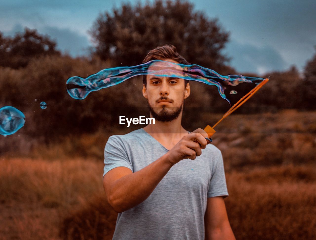 Portrait of man holding bubble wand on field