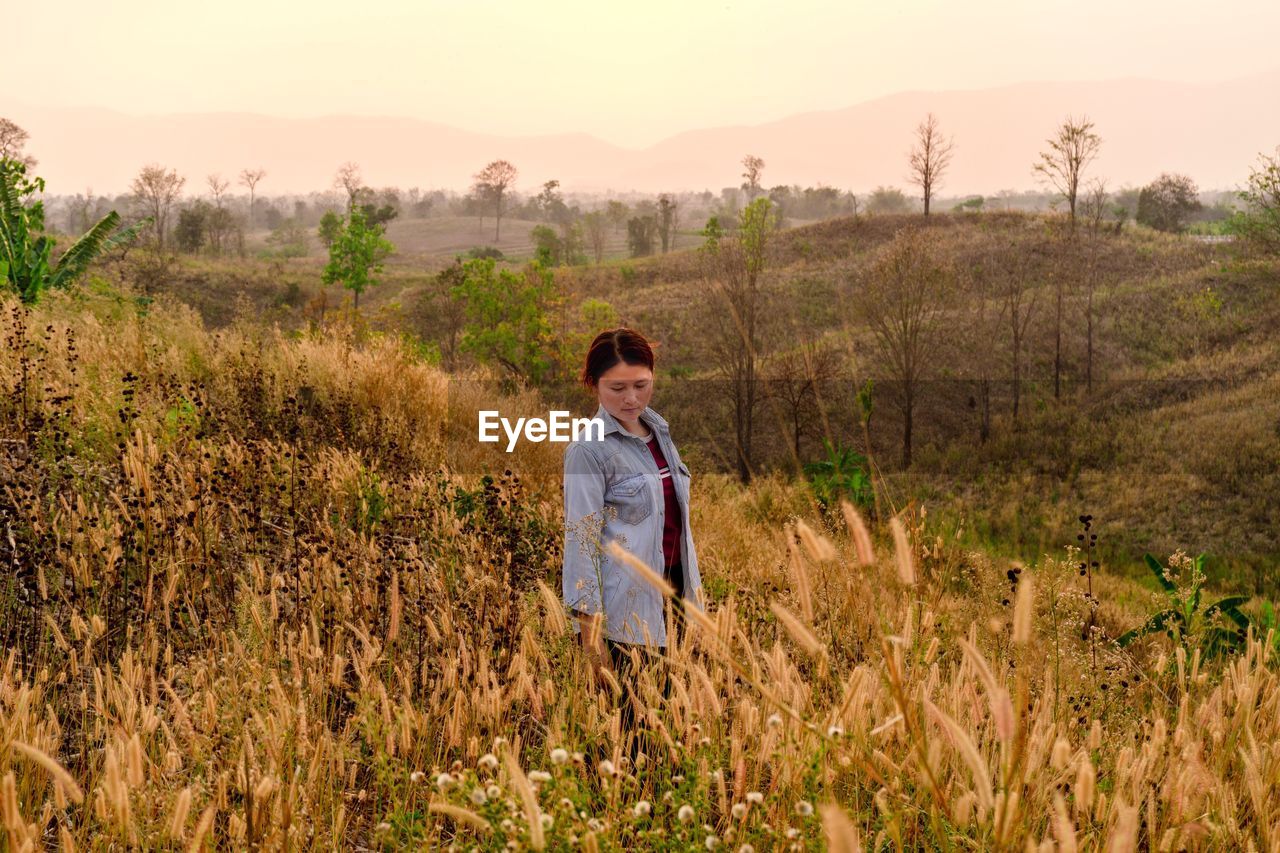 Woman looking down while standing by plants against landscape