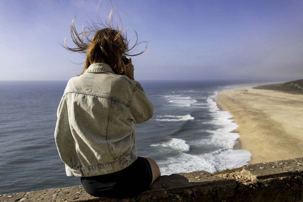 Rear view of woman photographing sea against sky