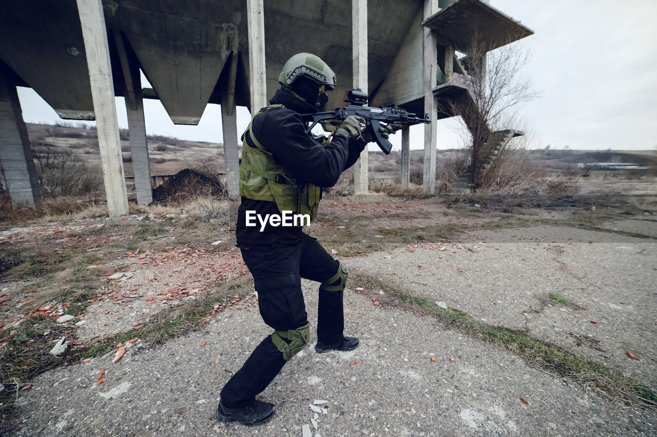 Army soldier aiming while standing against built structure