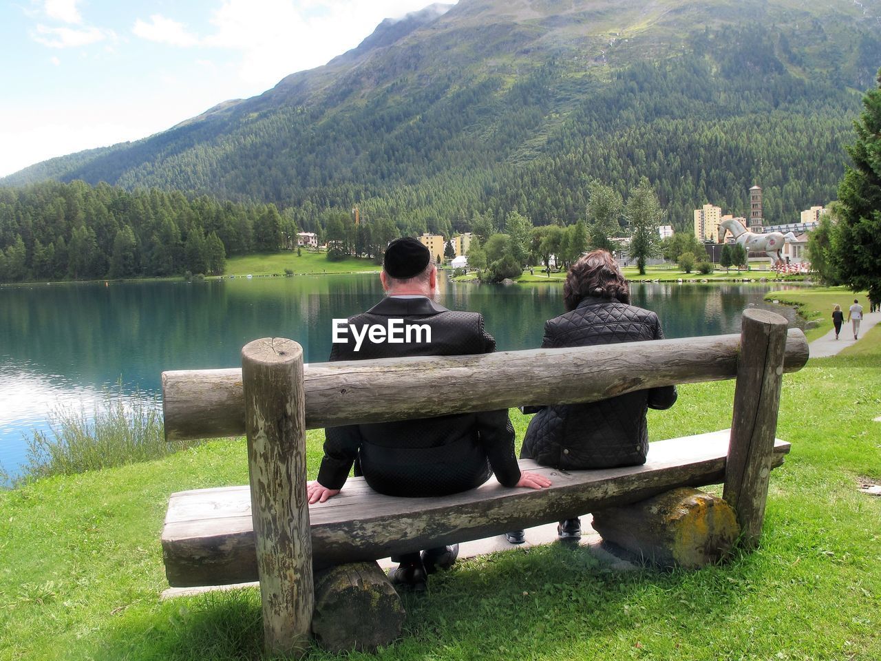 Rear view of men sitting by lake against mountain