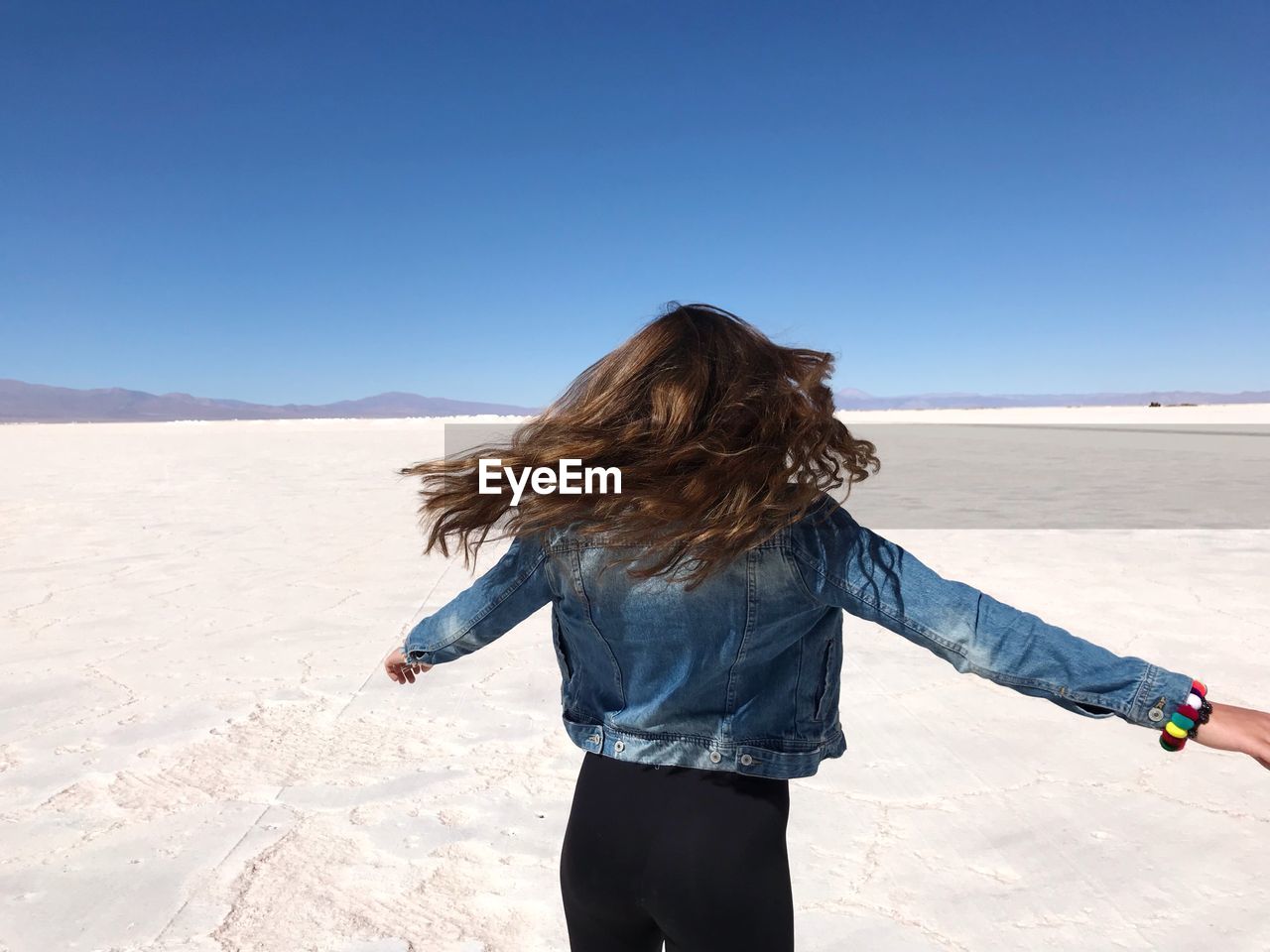 Rear view of playful woman spinning on land against clear blue sky during sunny day