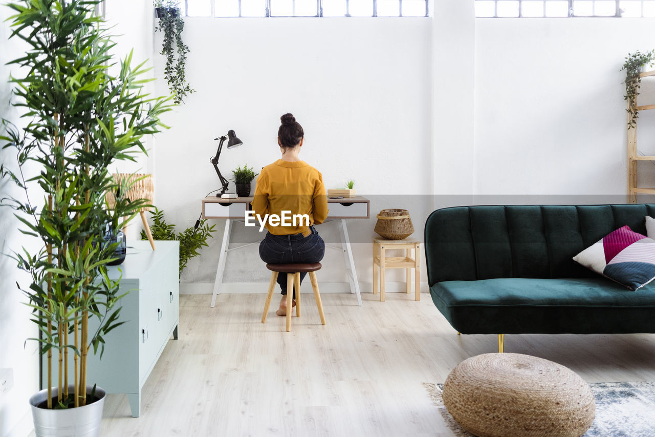 Young woman working while sitting on stool at home office