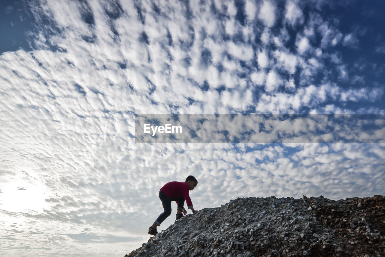 Side view of boy climbing mountain against cloudy sky