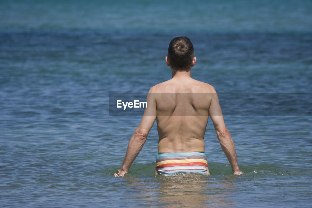 Rear view of shirtless man at sea