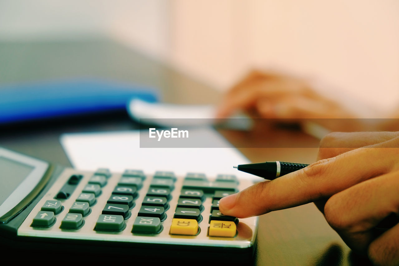 Close-up of hand using calculator on table