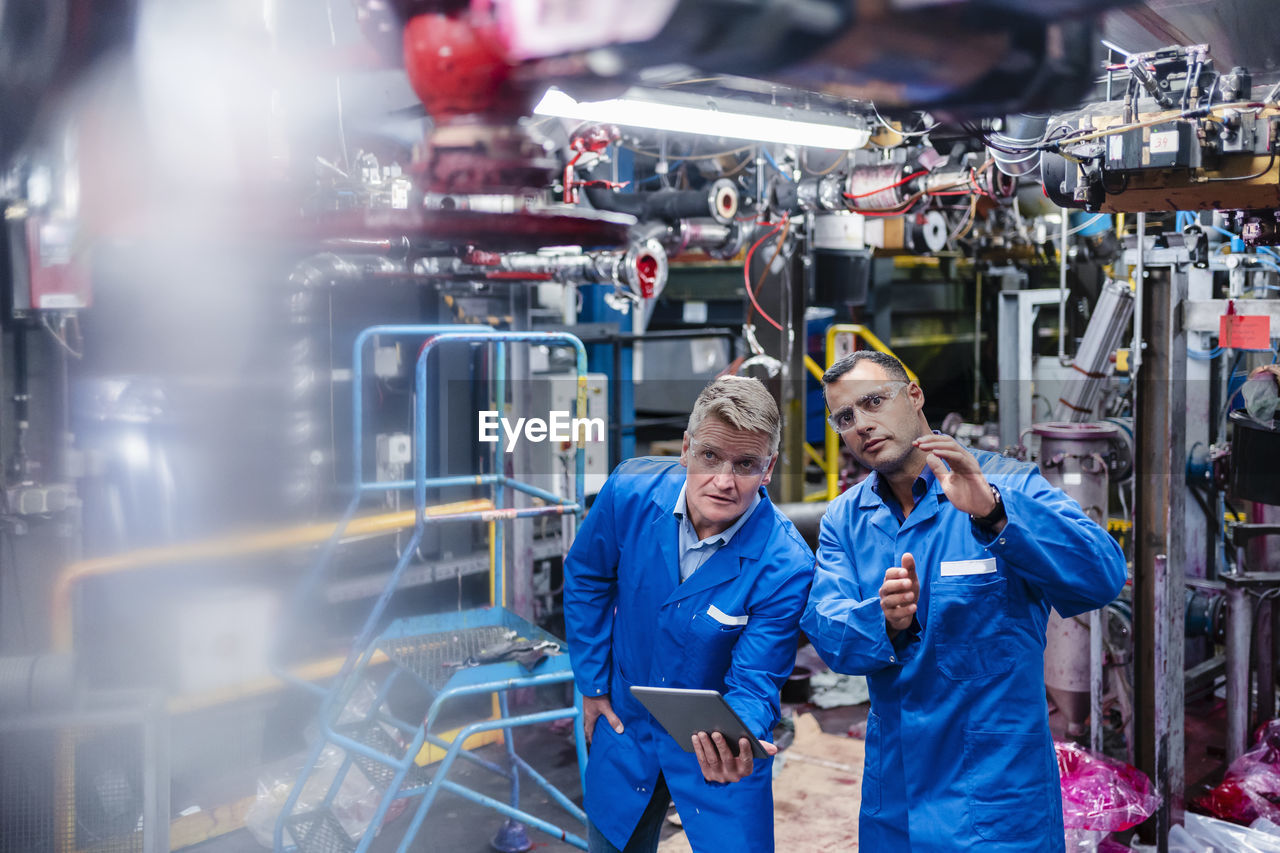 Male technician explaining strategy to colleague with digital tablet in industry