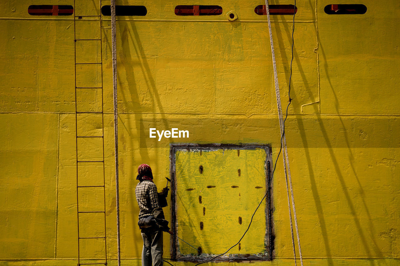 Rear view of worker painting wall outdoors