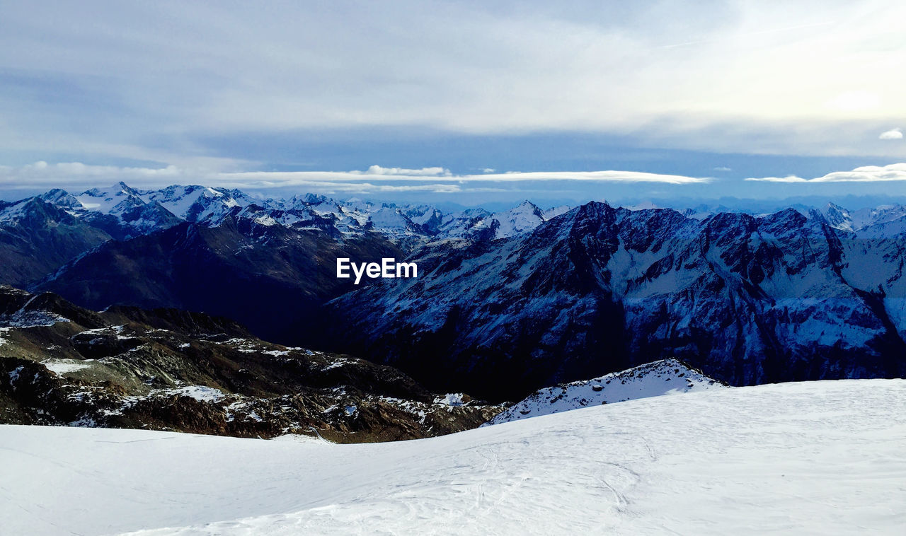 Scenic view of snow covered mountains against cloudy sky