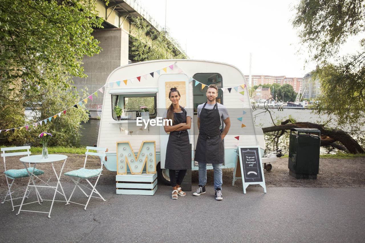 Full length portrait of confident owners standing outside food truck on street