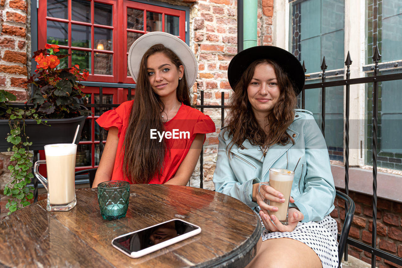 Two cheerful pretty young women drinking coffee, talking and laughing in outdoor cafe