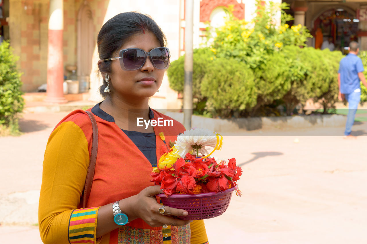 Bengali woman holding a bucket of religious offering flowers during durga puja celebration.