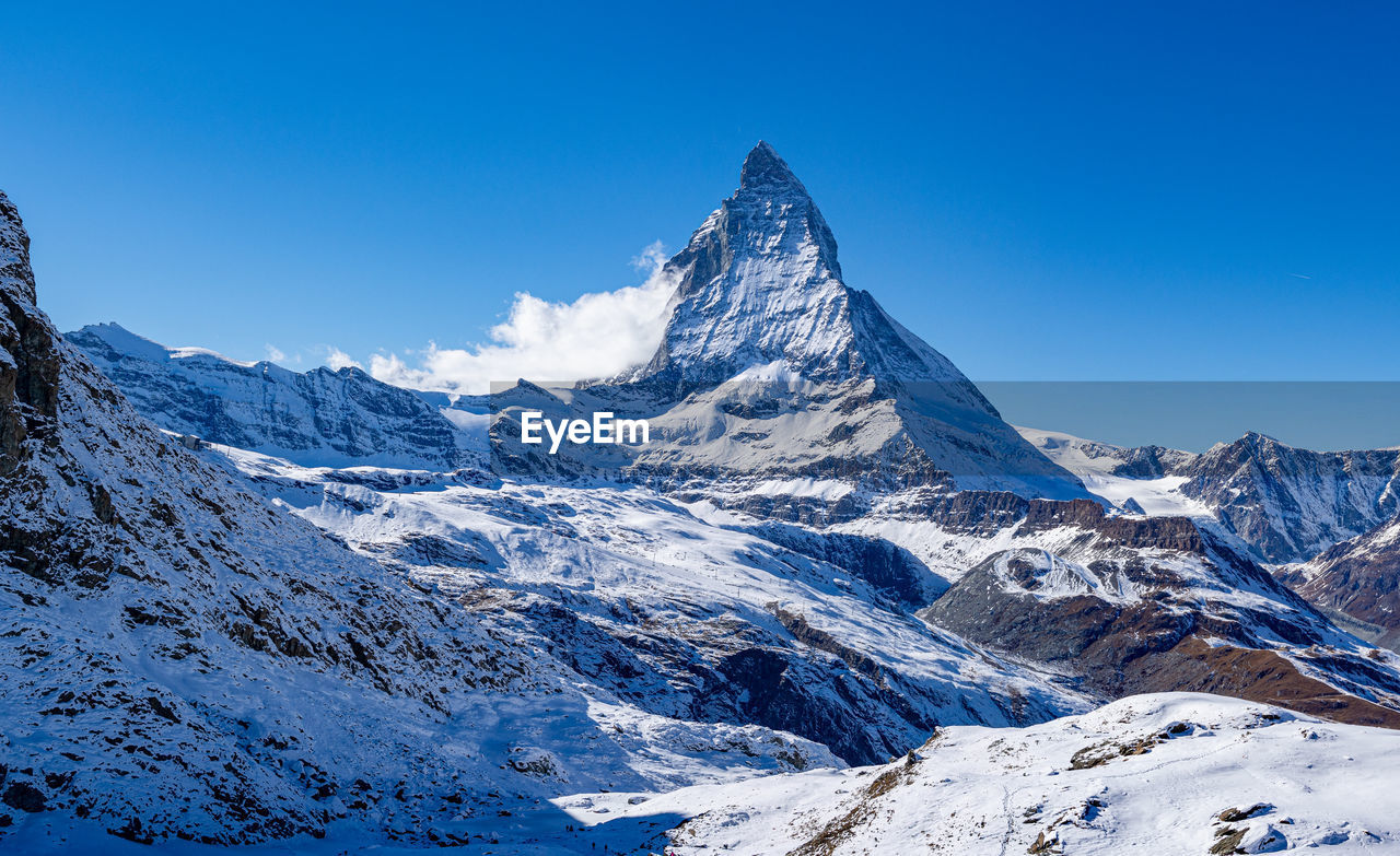 Scenic view of the matterhorn and surrounding snowcapped mountains against clear blue sky