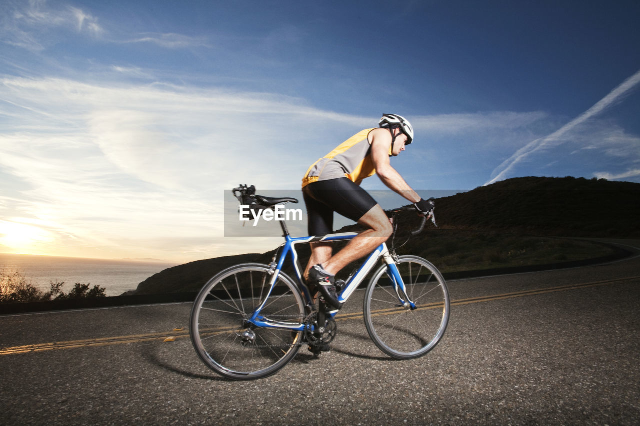 Side view of cyclist riding bicycle on road against sky