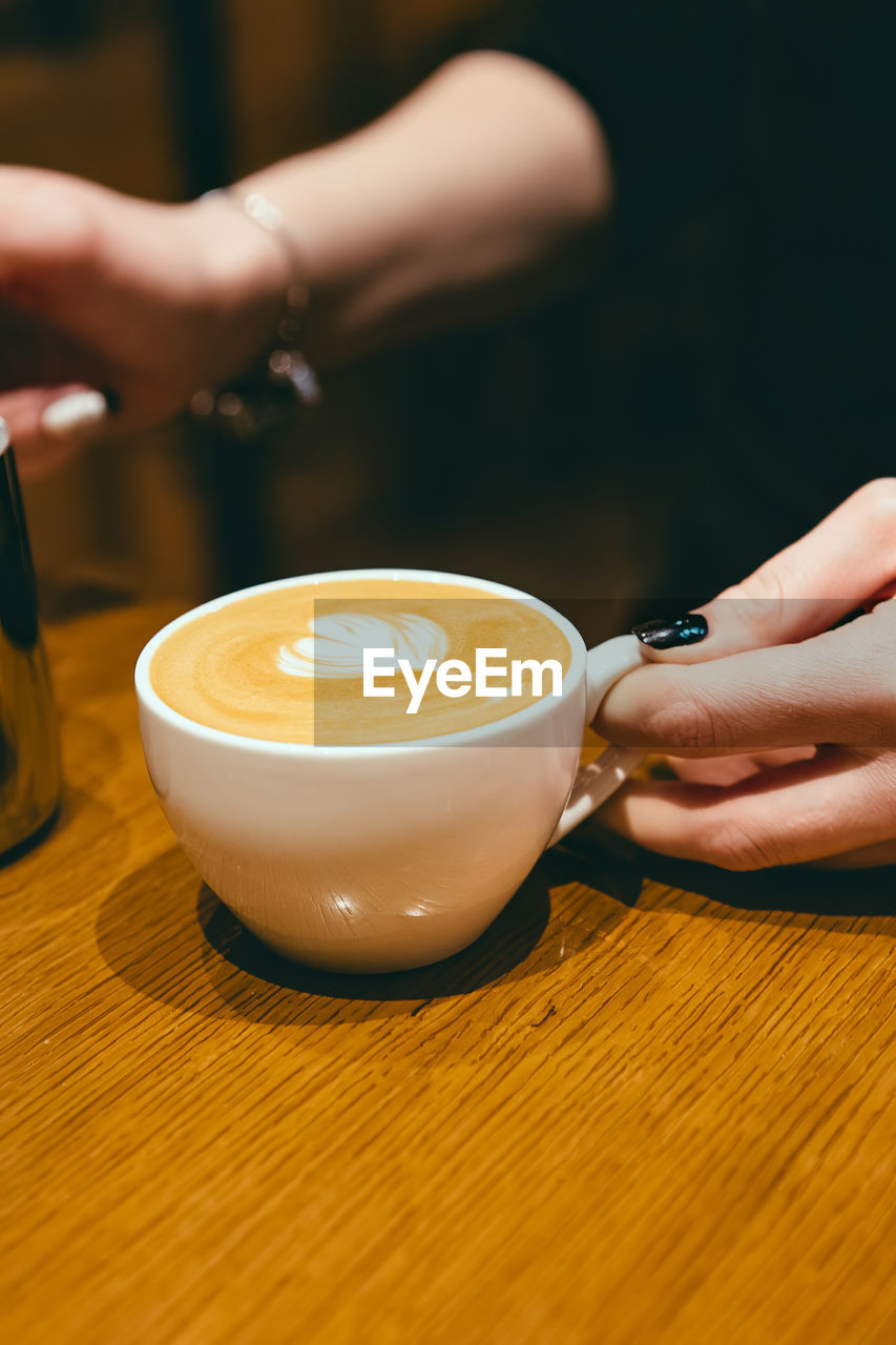 Midsection of woman holding coffee cup on table