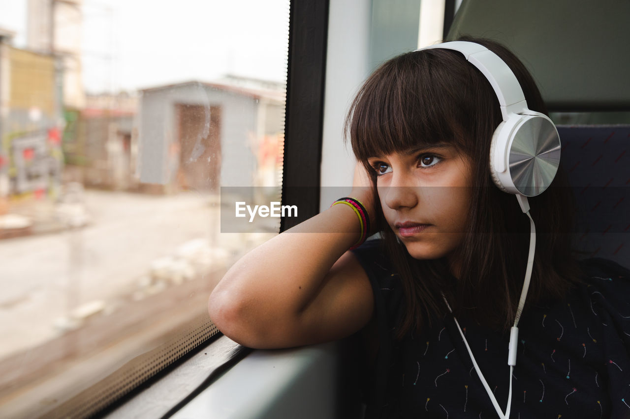 Thoughtful girl looking through window while listening music in train