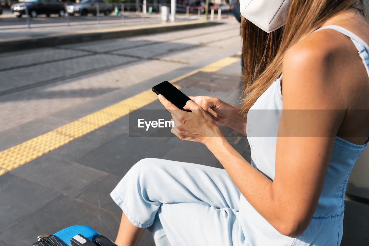 MIDSECTION OF WOMAN USING MOBILE PHONE WHILE SITTING ON CAR