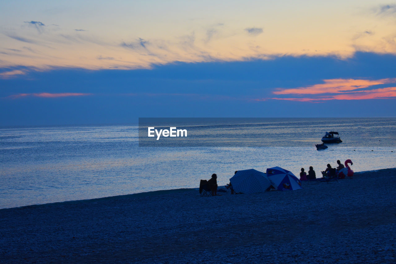 People on beach against sky during sunset