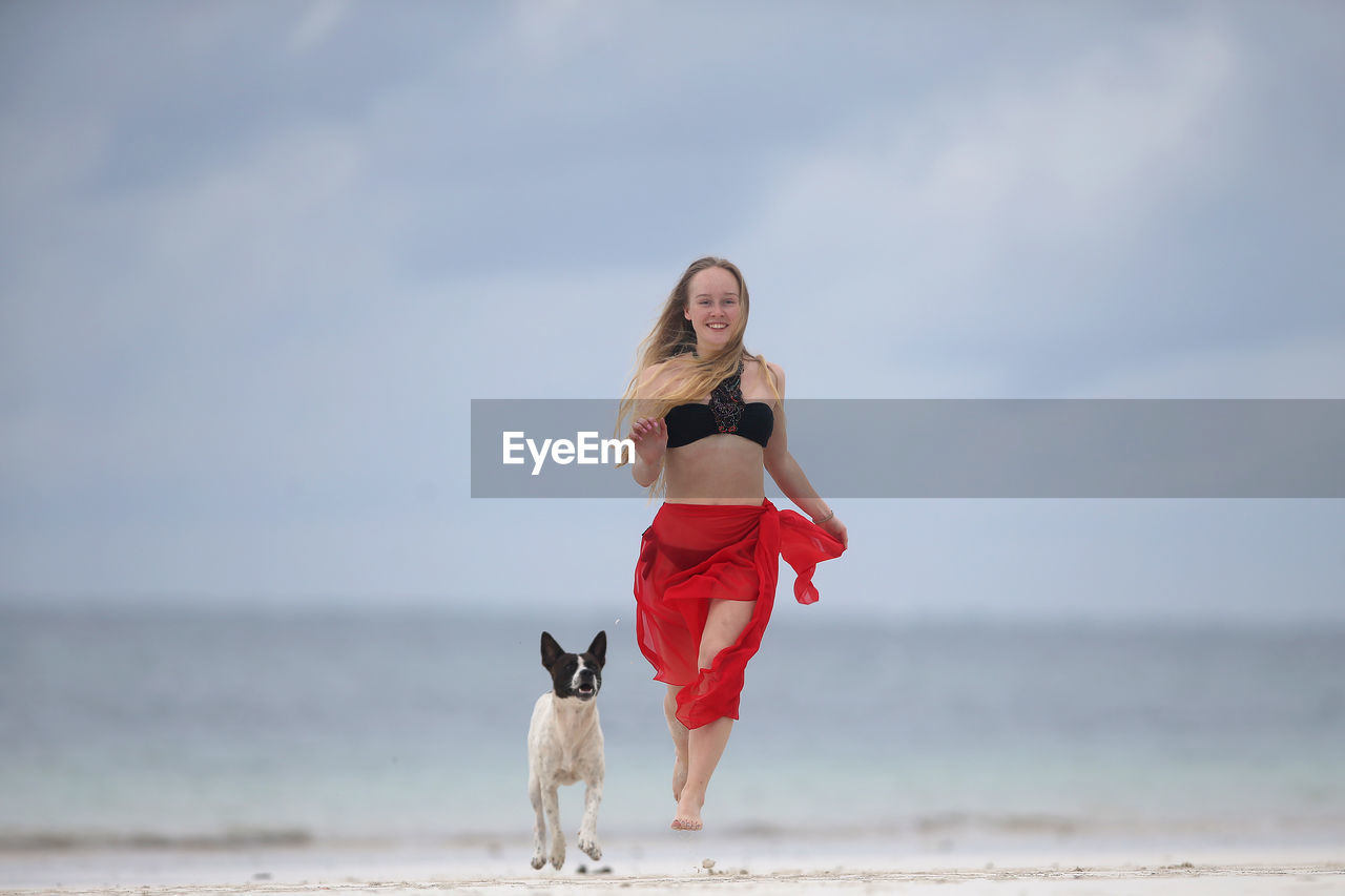 Full length of woman with dog jumping at beach