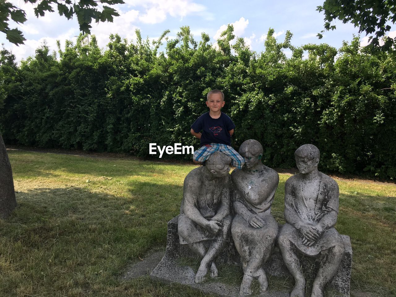 PORTRAIT OF GIRL SITTING BY STATUE AGAINST TREES