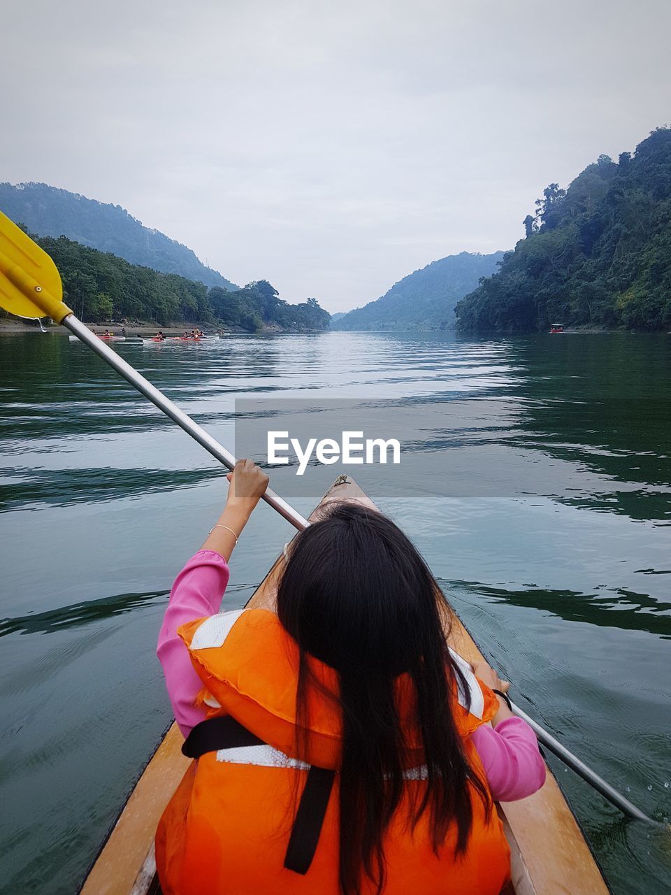 Rear view of woman kayaking in lake against sky