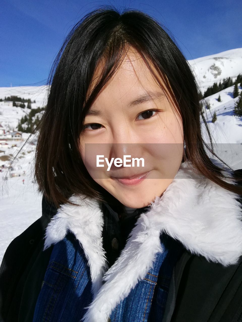 Close-up portrait of smiling young woman standing on mountain during winter