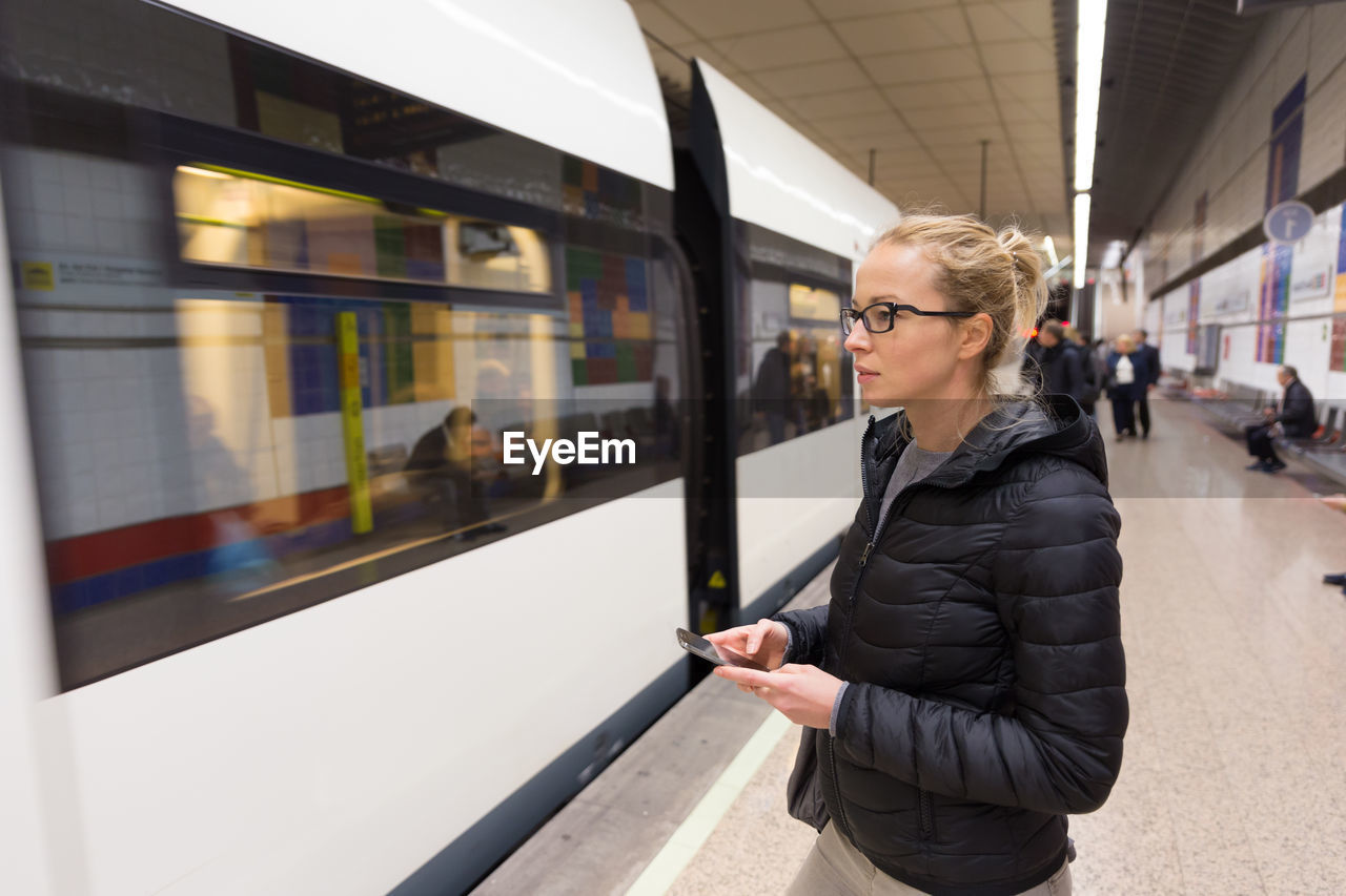 Side view of woman using smart phone standing at railroad station platform