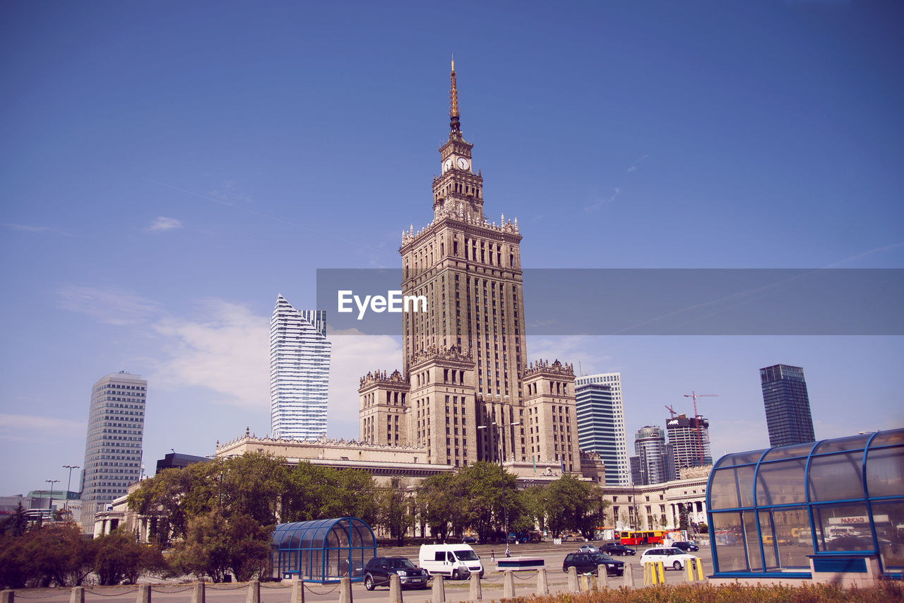 Palace of culture and science by street against blue sky