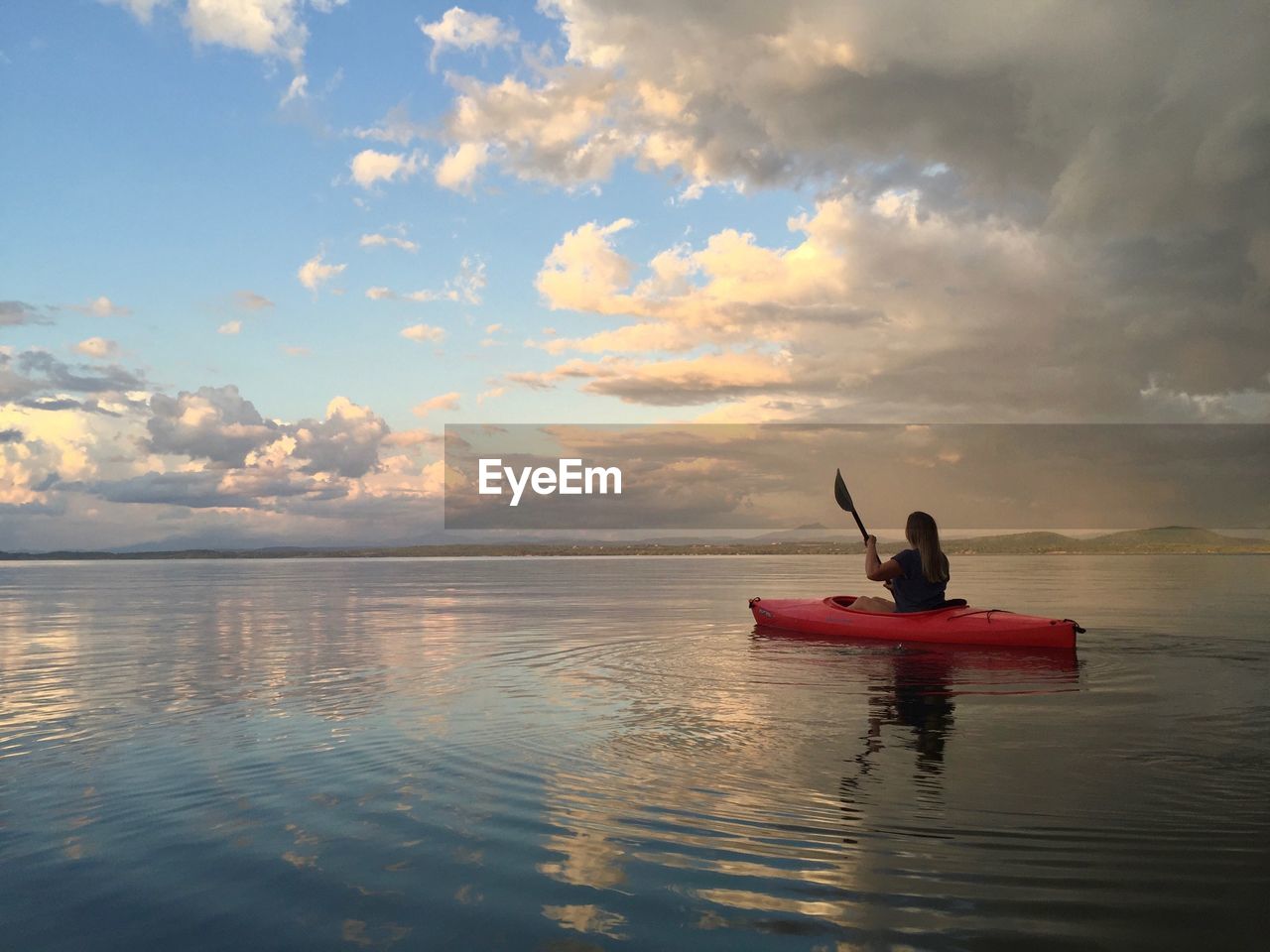 Mature woman canoeing on sea against cloudy sky during sunset