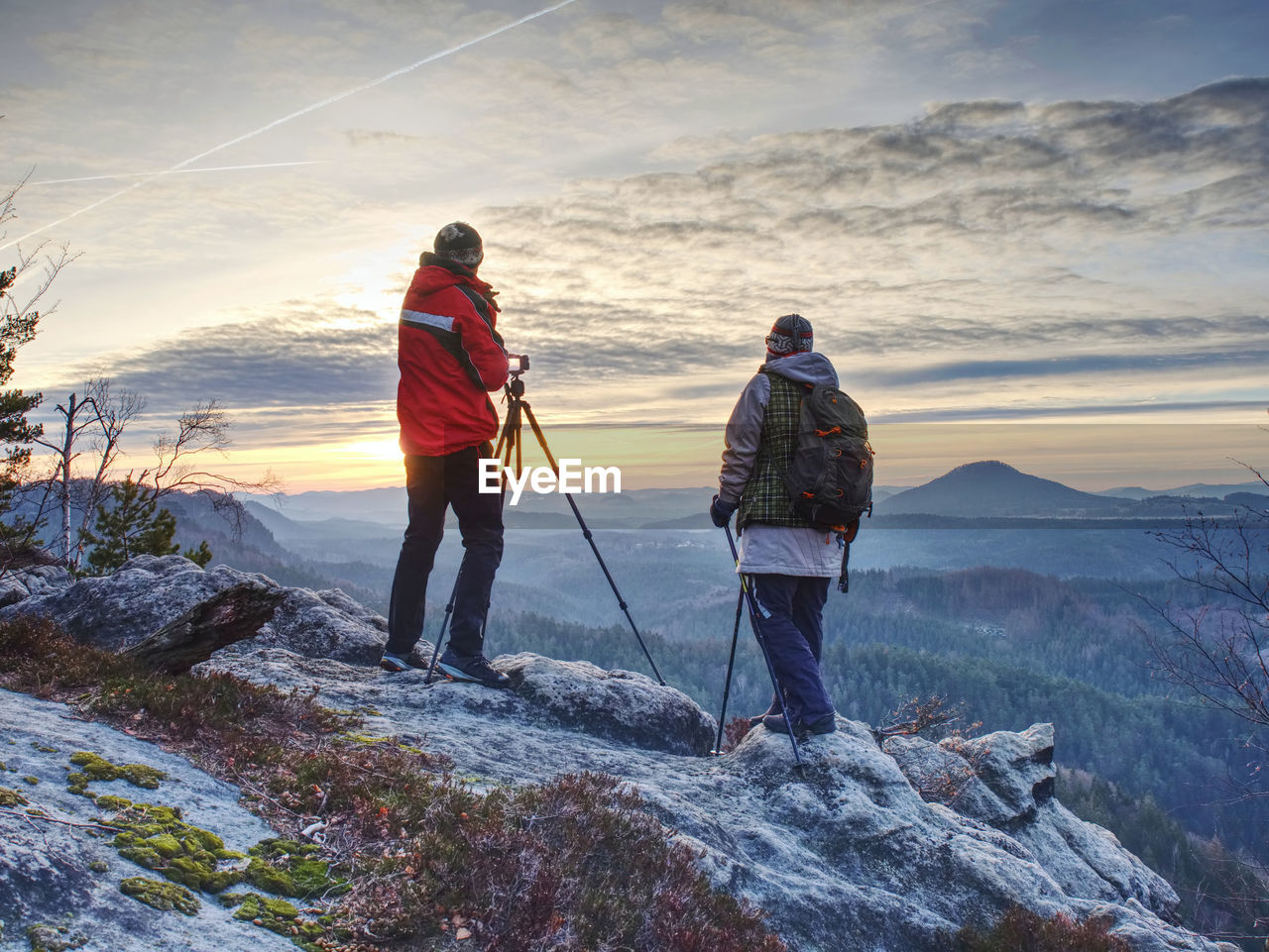 REAR VIEW OF MAN STANDING ON ROCK AGAINST SKY