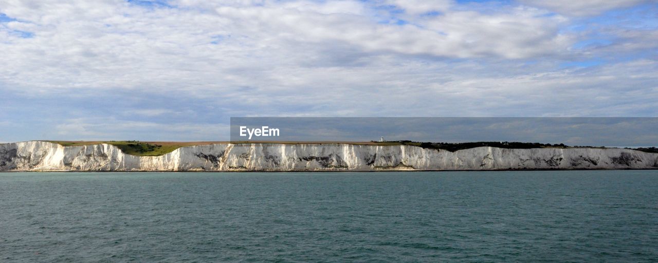 Scenic view of sea by white cliffs of dover against cloudy sky