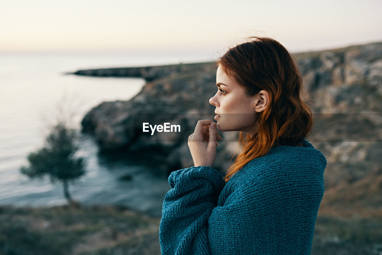 BEAUTIFUL YOUNG WOMAN STANDING ON ROCK AT SEA SHORE