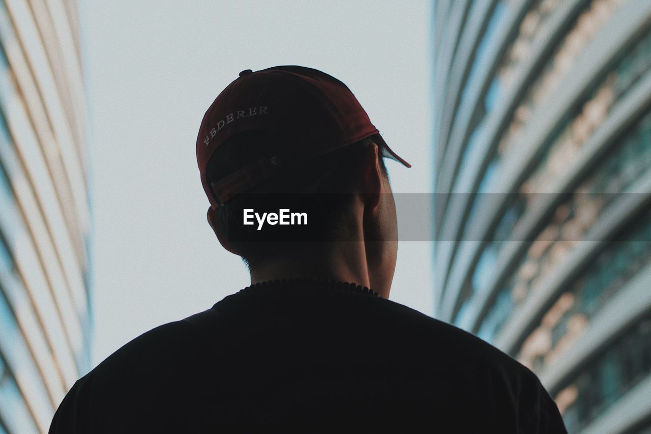 REAR VIEW PORTRAIT OF MAN WEARING HAT AGAINST BUILT STRUCTURE