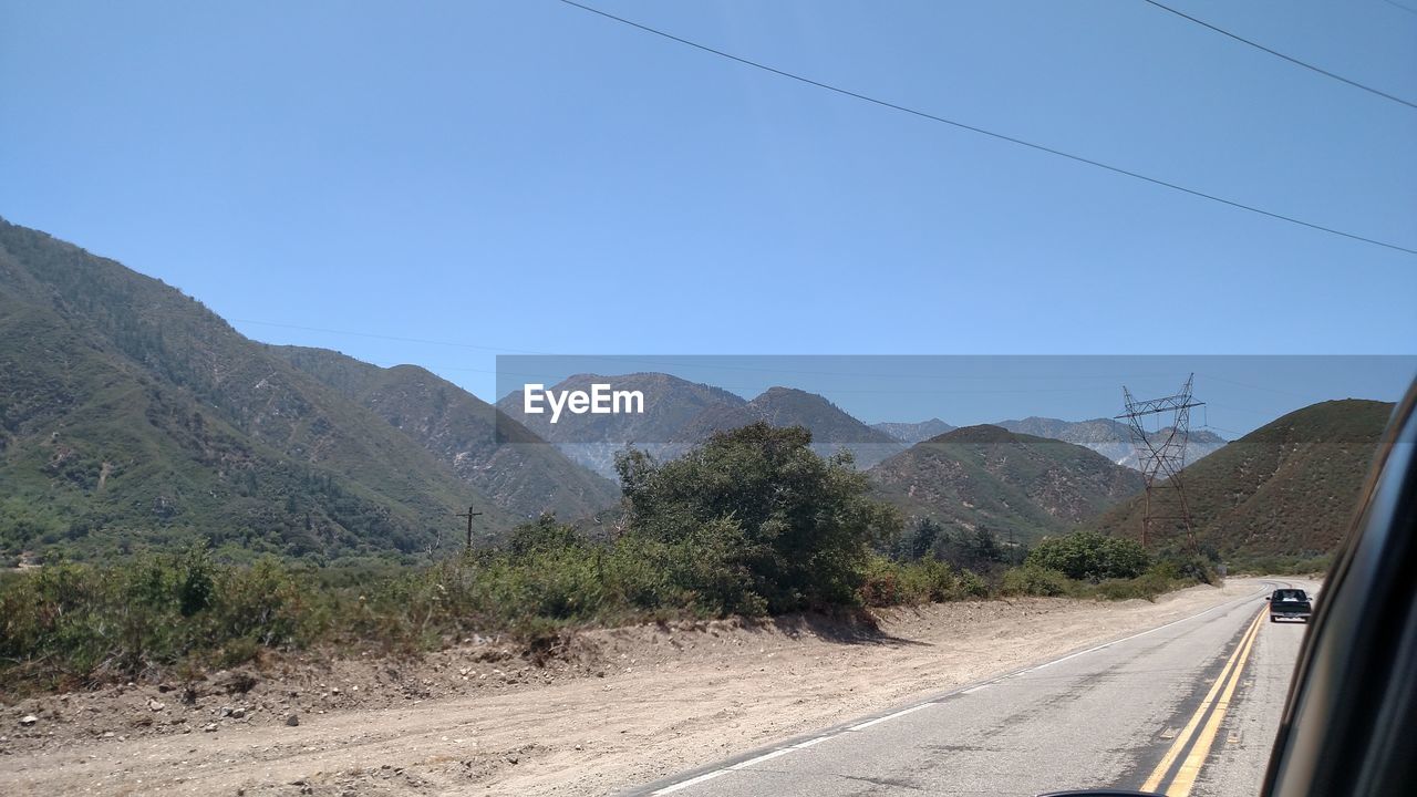 Road leading towards mountains against clear blue sky