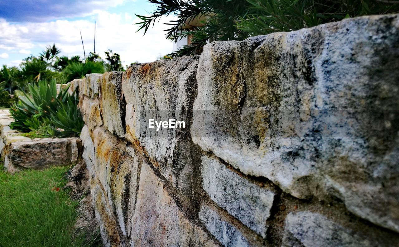 LOW ANGLE VIEW OF ROCKS ON WALL AGAINST TREES
