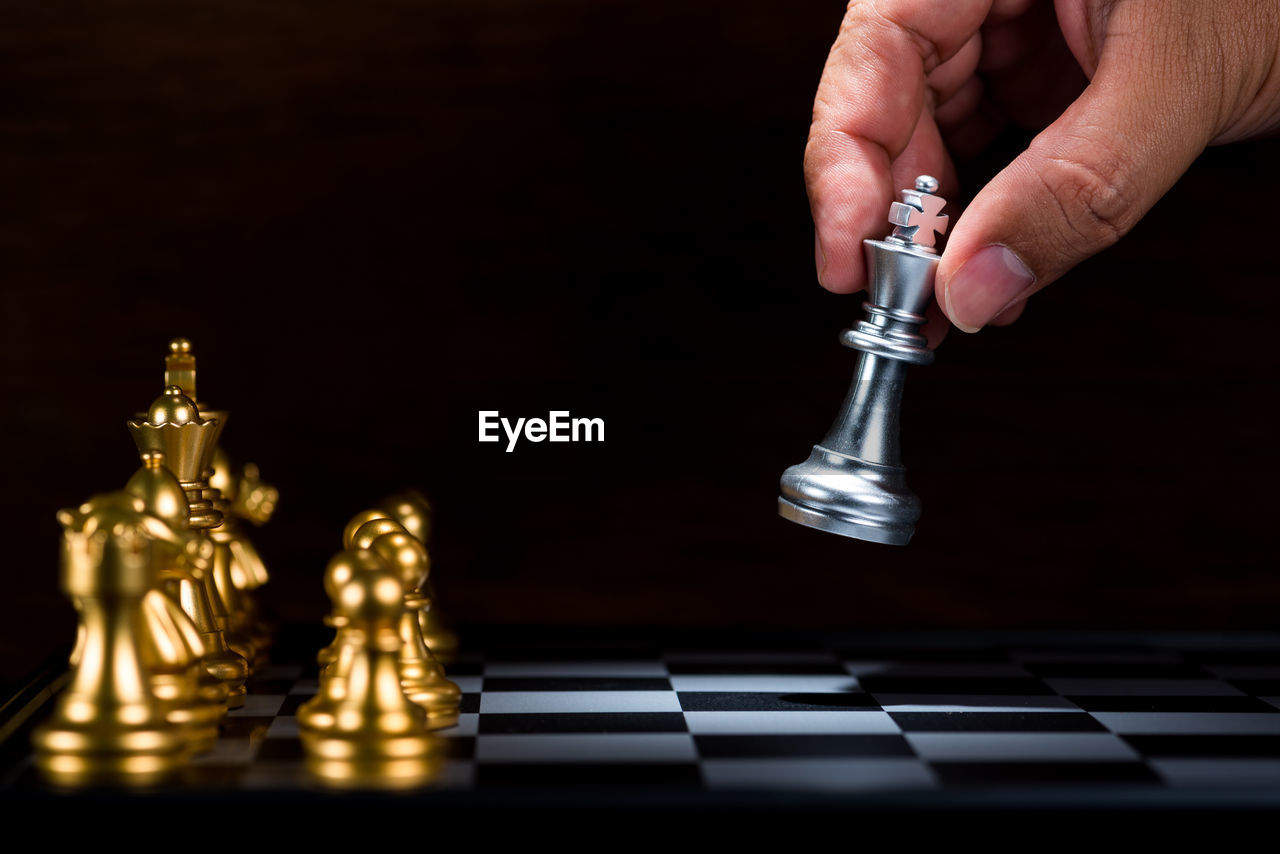 Cropped hand of person playing with chess against black background