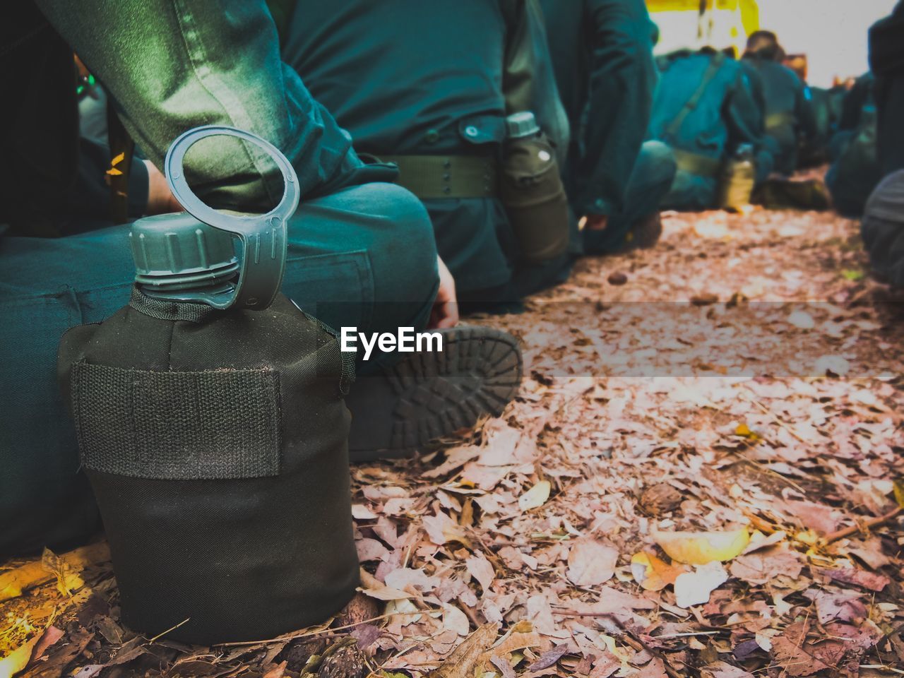 Close-up of water bottle by low section of army soldiers sitting outdoors