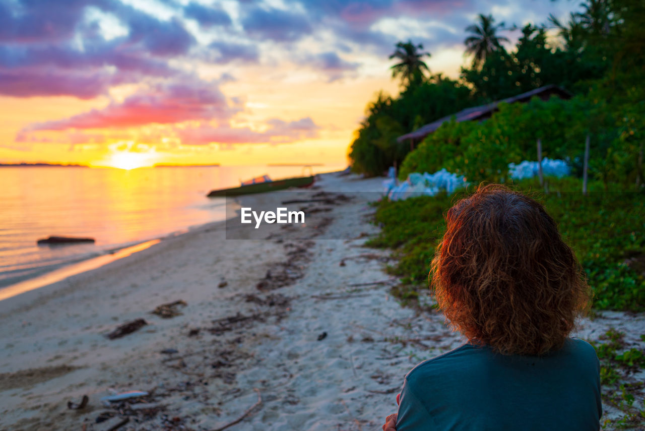 REAR VIEW OF WOMAN ON BEACH DURING SUNSET