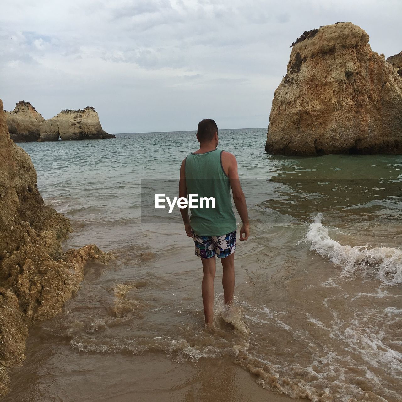 REAR VIEW OF MAN WALKING ON ROCK FORMATION AT SEA