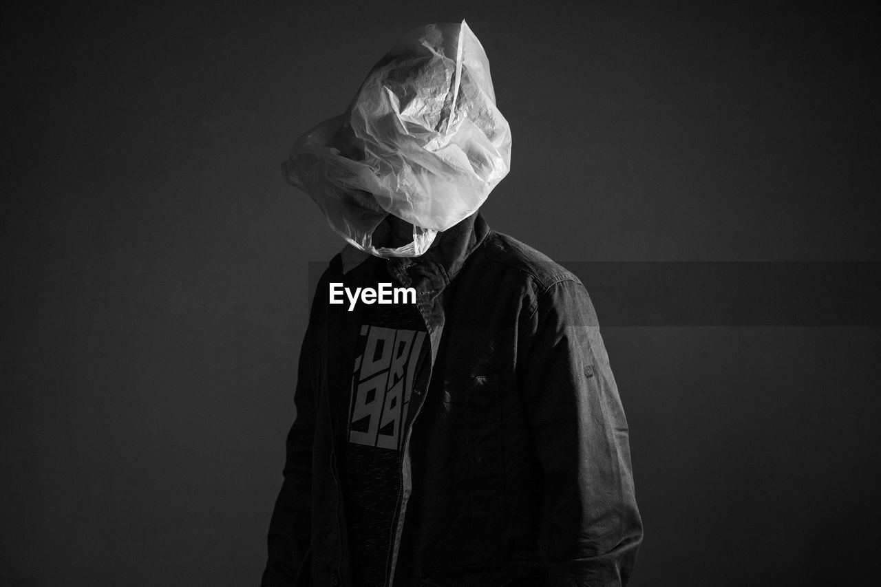 MIDSECTION OF MAN WEARING MASK AGAINST BLACK BACKGROUND